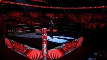 WWE RAW arena with red lighting and a speaker standing in the center of the wrestling ring.